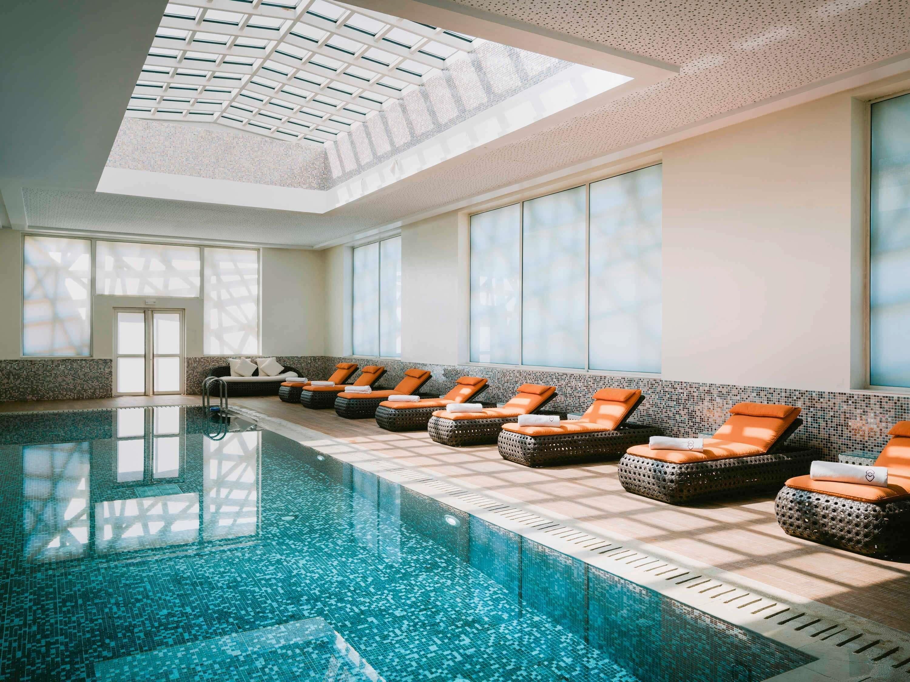A swimming pool with lounge chairs, a skylight, and a tiled floor.