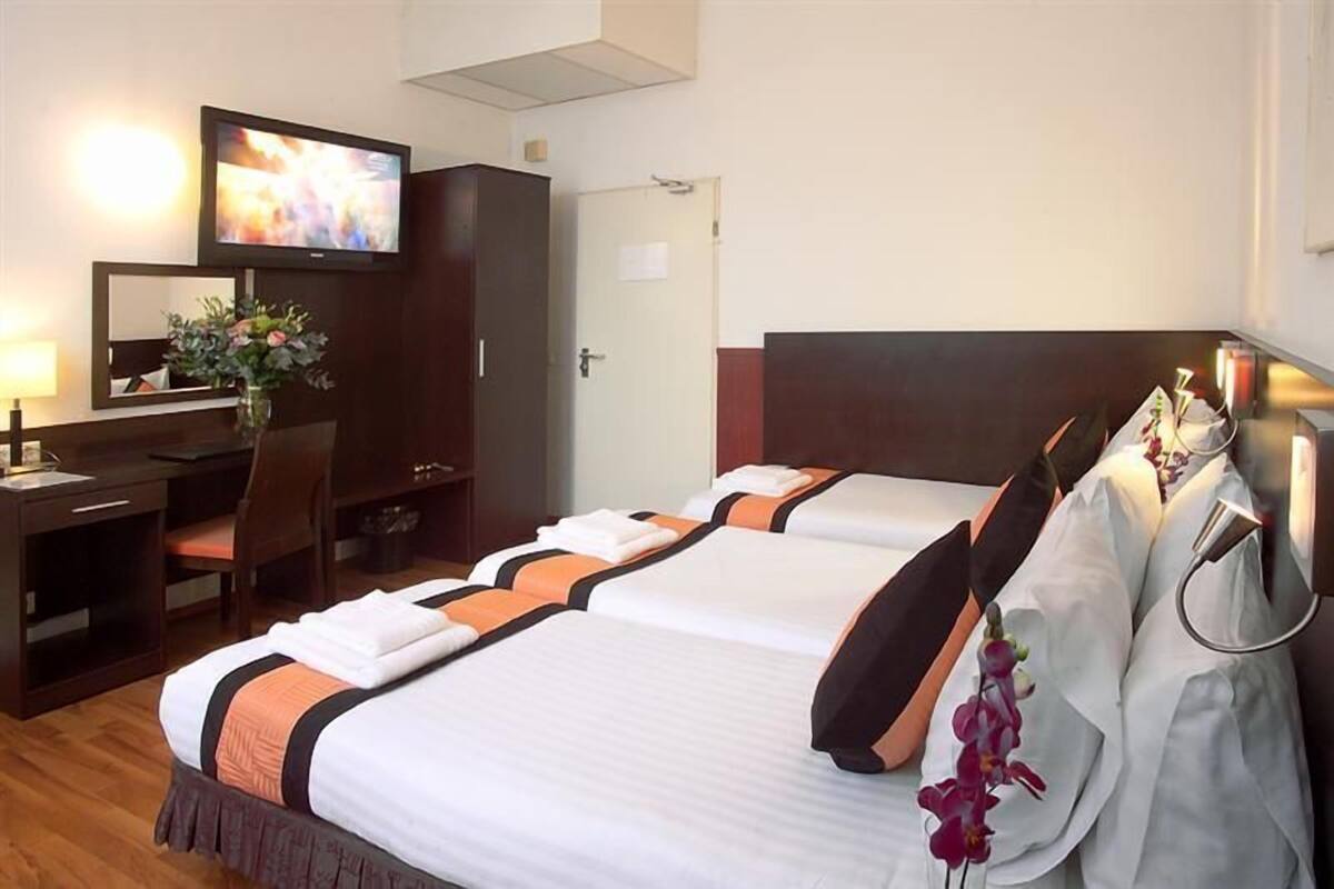A hotel room with two beds, a desk, a TV, and a mirror.