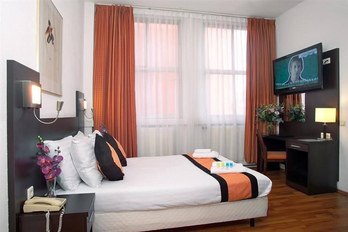 A hotel room with a bed, a desk, a television, and a telephone.