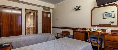 A hotel room with two single beds, a desk with a chair, a television, and a mirror.