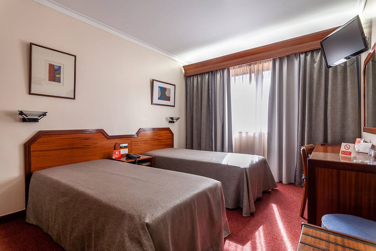 A hotel room with two beds, a desk, a television, and two framed pictures on the wall.