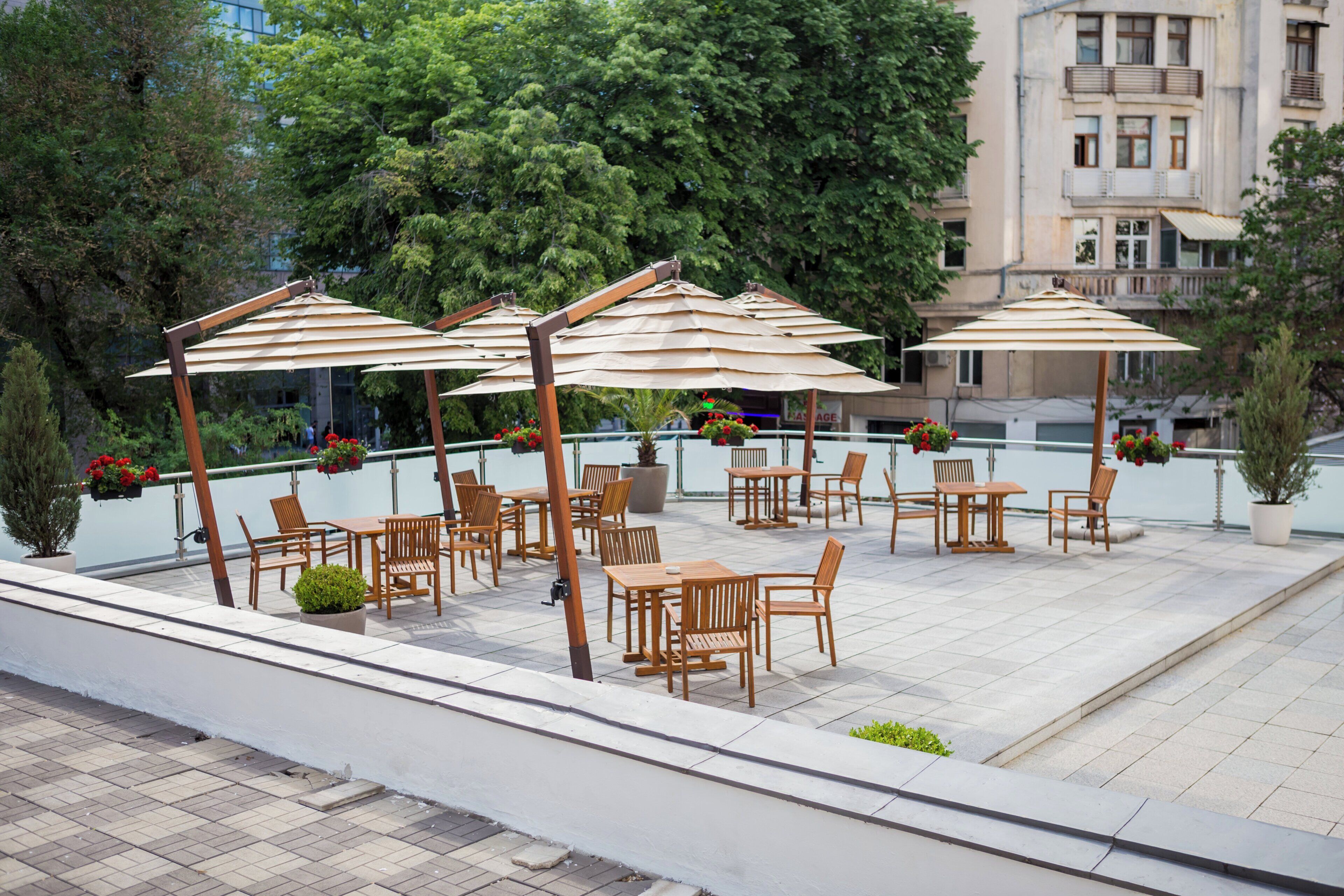 Un espace extérieur aménagé avec des tables et des chaises en bois, des parasols et des plantes en pot.