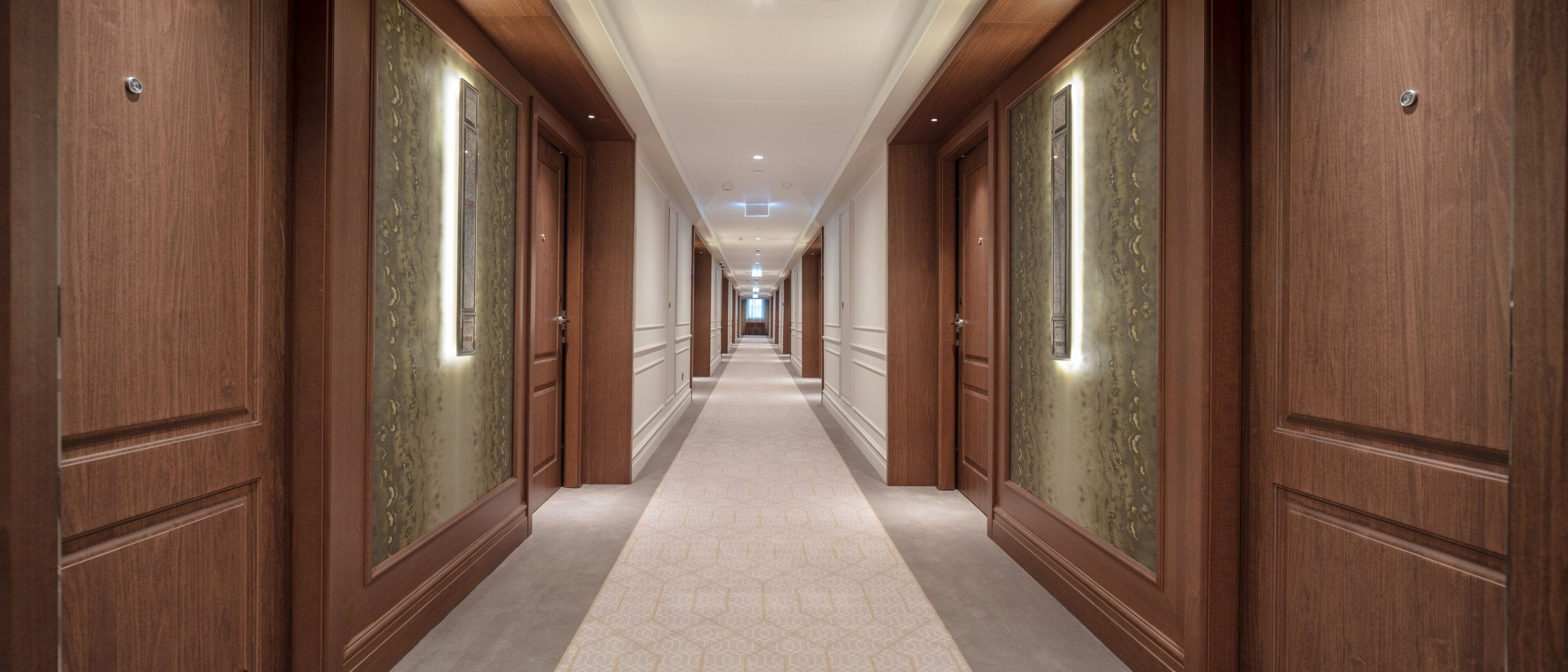 Un long couloir étroit, avec des portes en bois et un tapis à motifs.