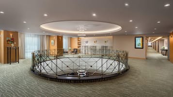 Un hall d’hôtel doté d’un garde-corps circulaire en verre au centre, d’un comptoir d’accueil et d’un couloir menant aux chambres.