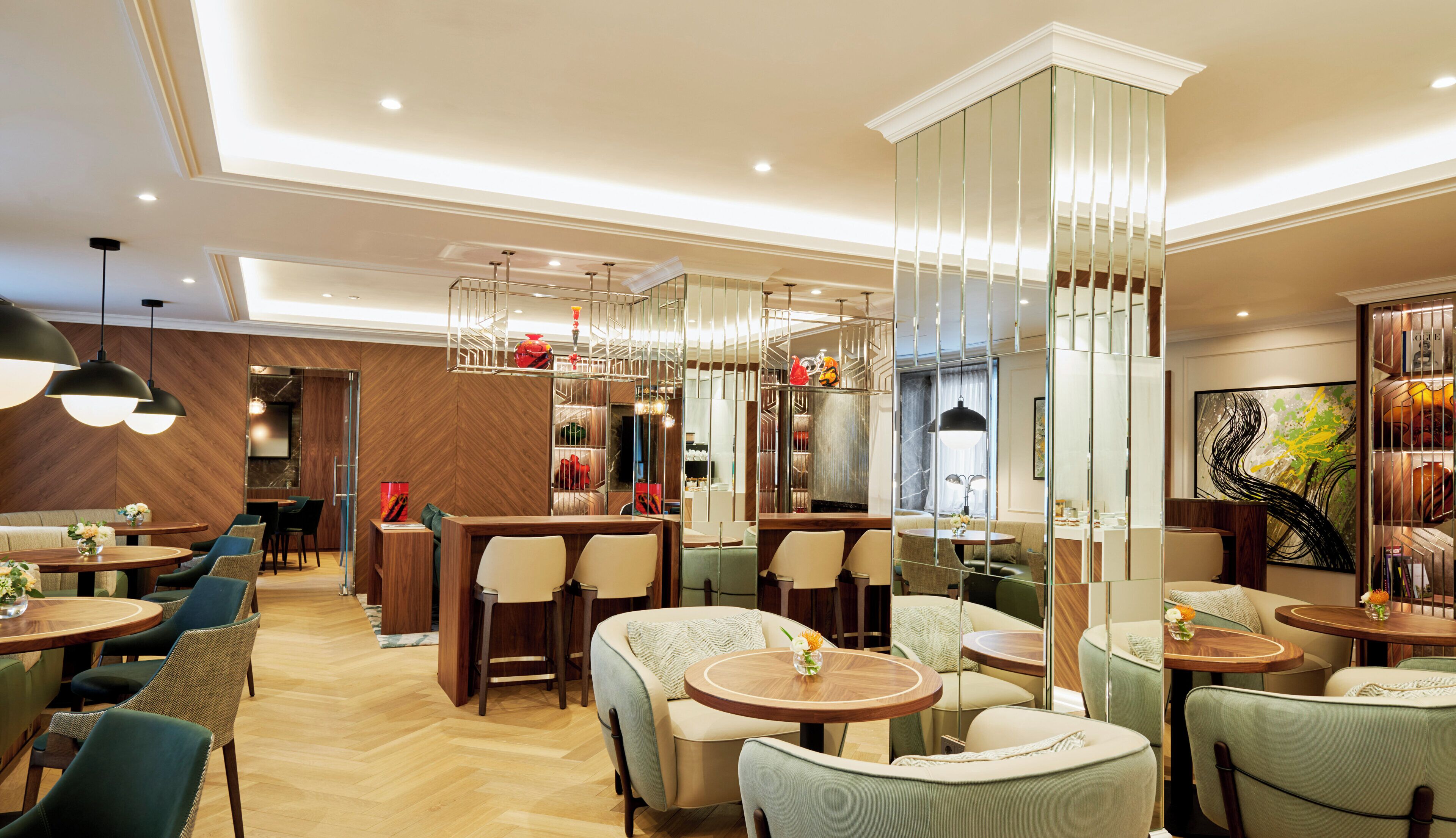 Un moderno vestíbulo de hotel con varias zonas de estar, incluyendo mesas redondas y sofás, y una partición de vidrio decorativa en el centro.