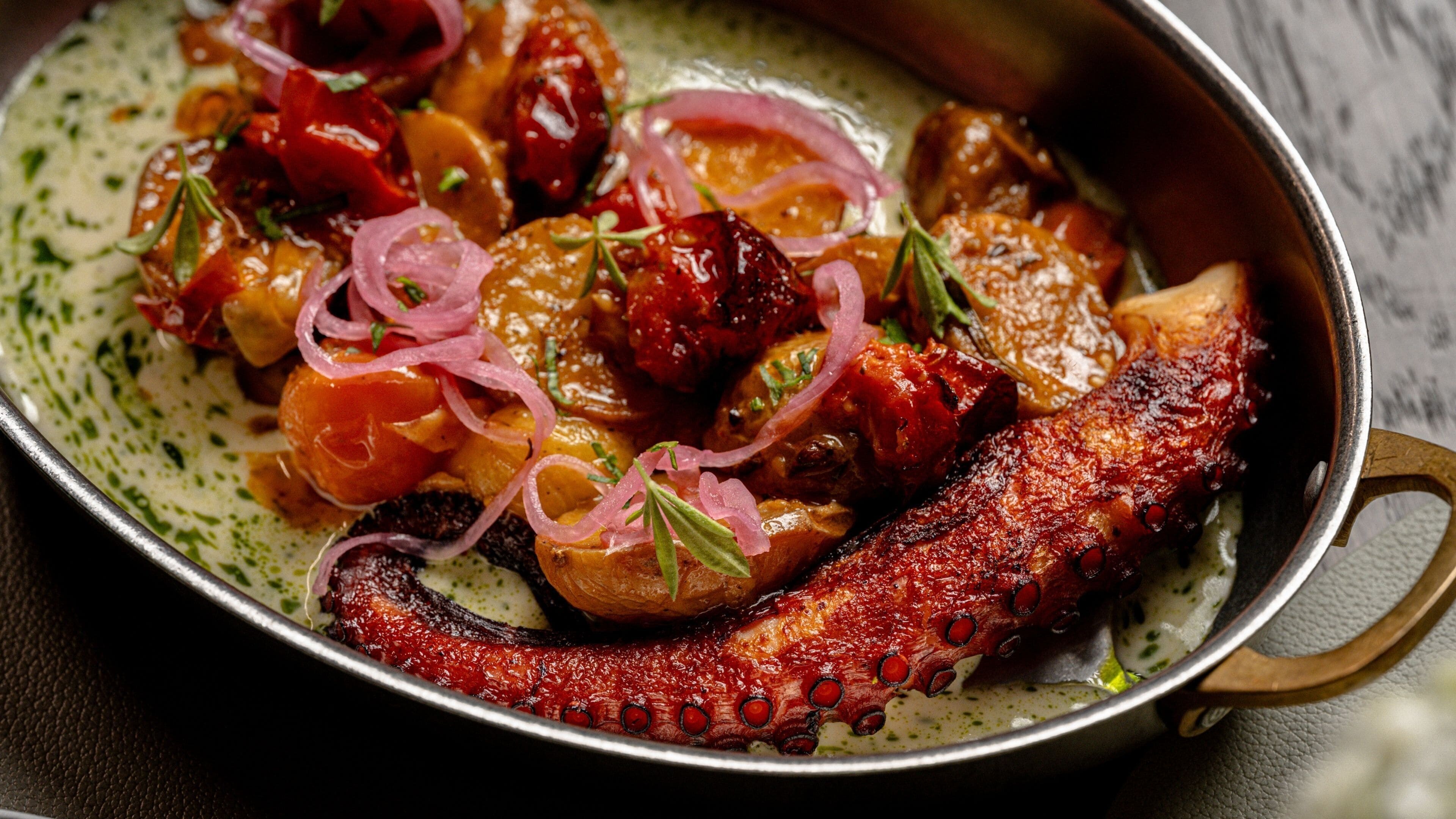 A dish with octopus, tomatoes, and onions in a pan.