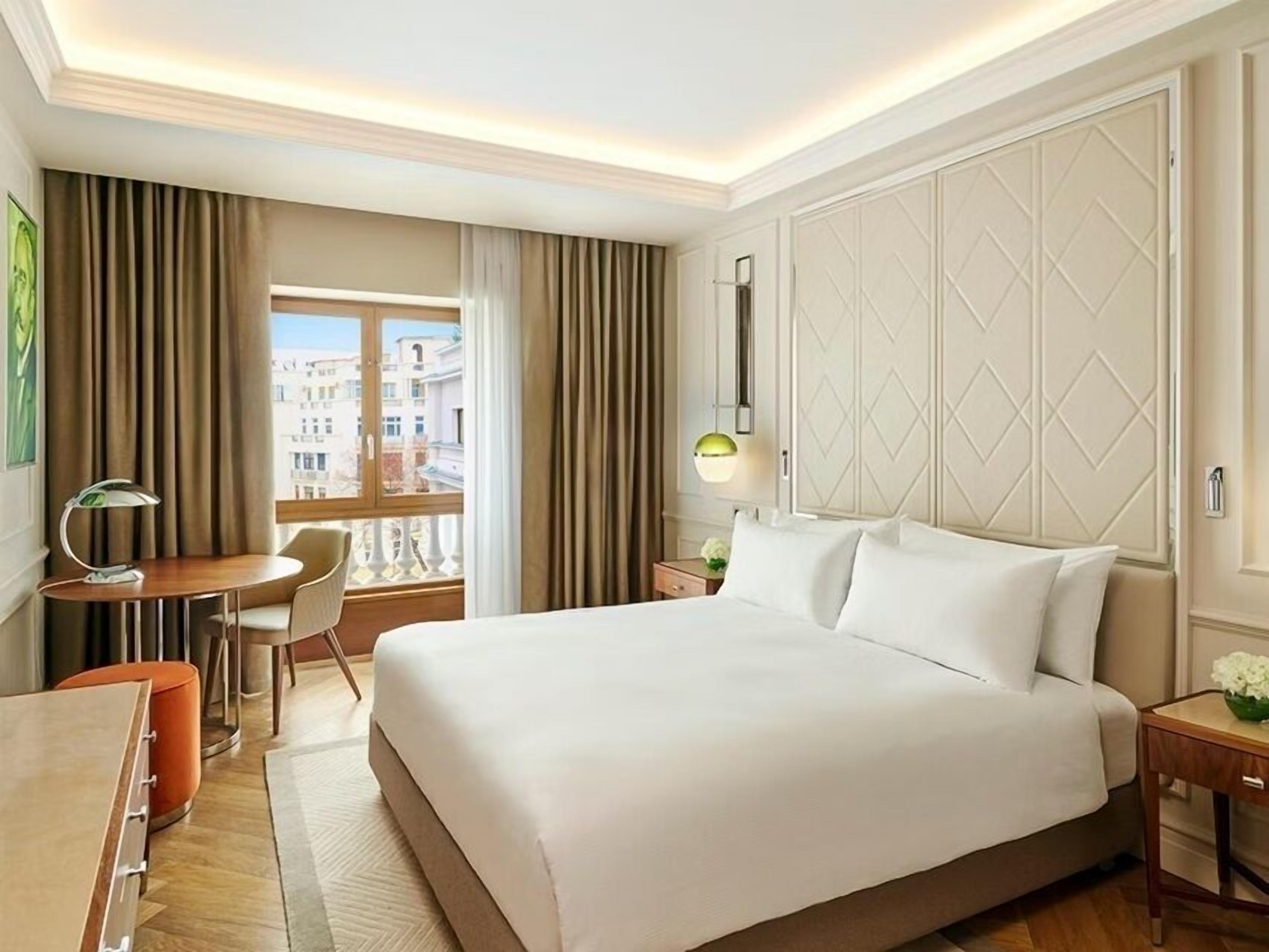 Habitació d'hotel amb un llit gran, una taula de treball, una cadira i vista a la ciutat des de la finestra.
