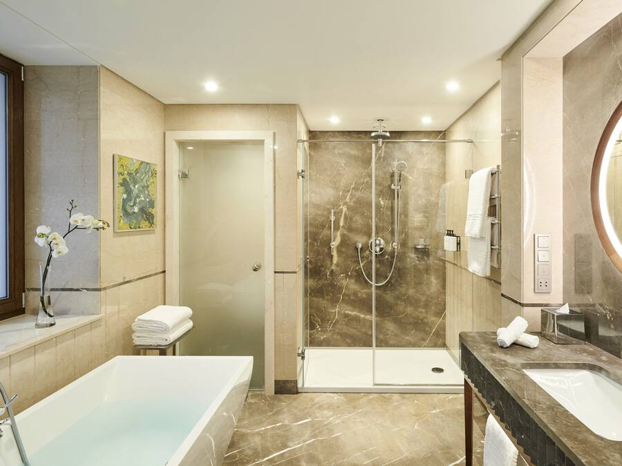A modern bathroom with a bathtub, two sinks, a walk-in shower, and a large mirror.