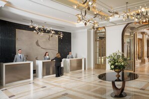Een hotel receptie met drie medewerkers, een groot abstract schilderij en een kroonluchter.
