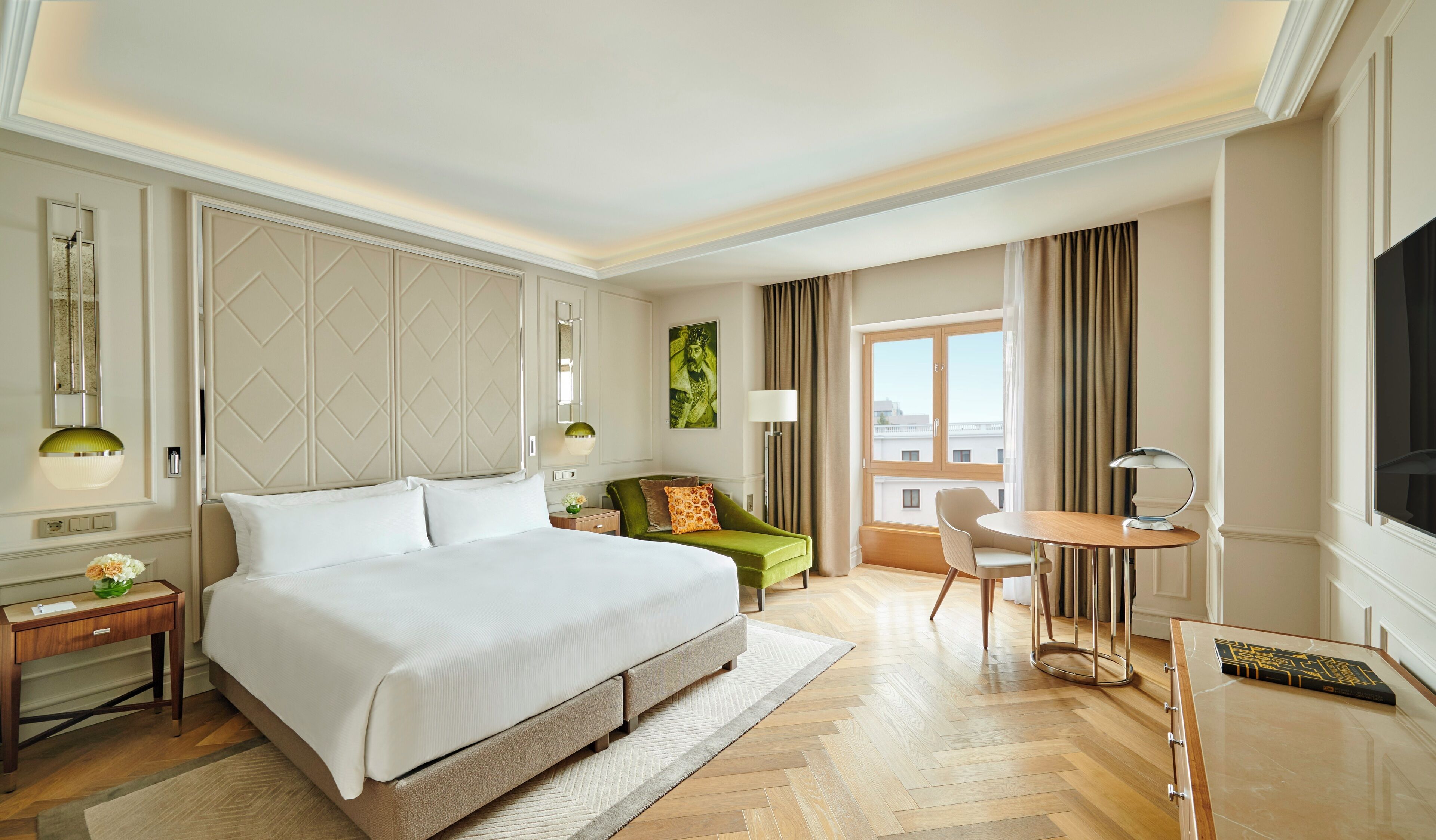 Une chambre d’hôtel avec un grand lit, un fauteuil vert, une petite table et un téléviseur.