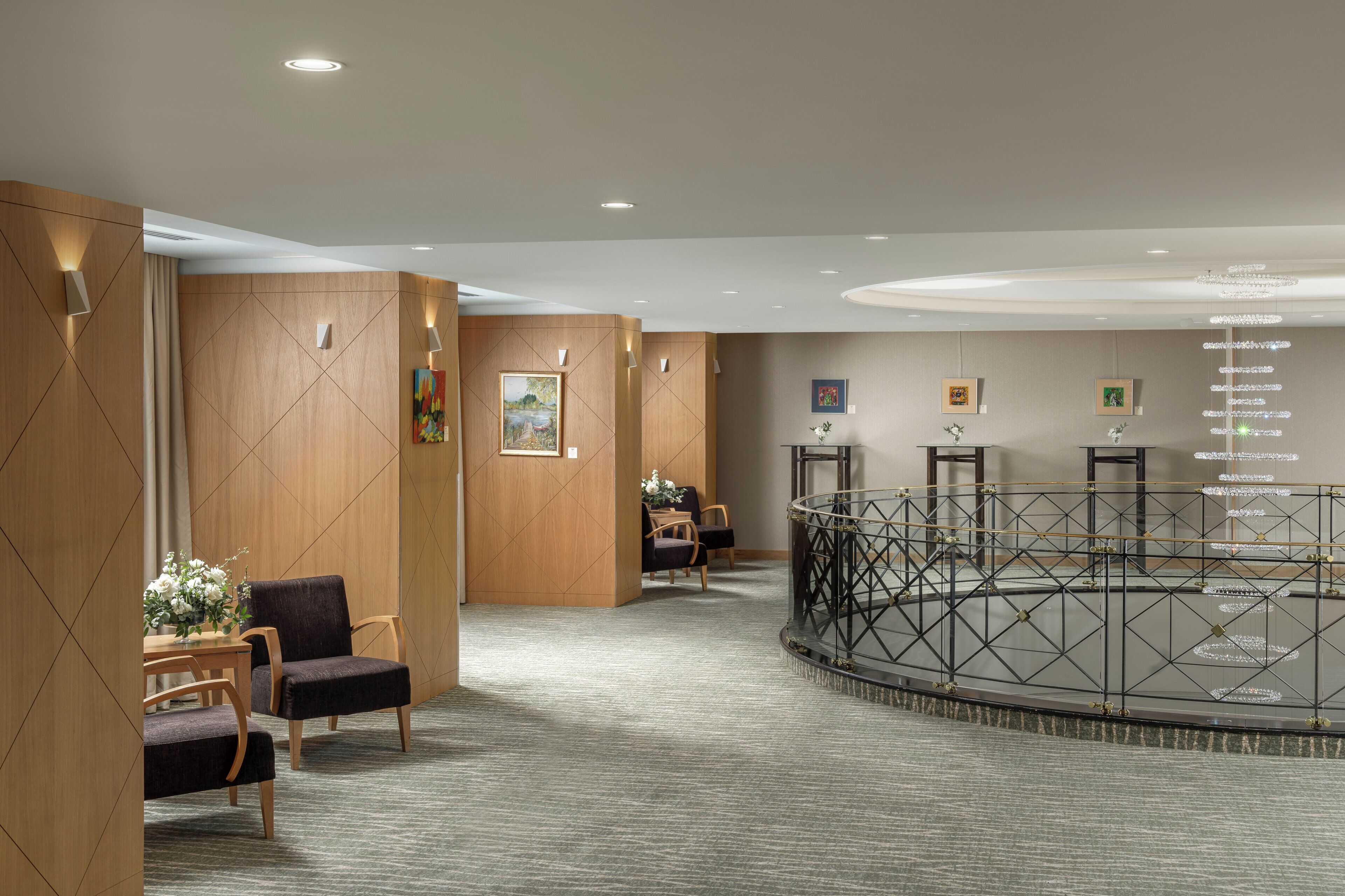 A hotel lobby with a central glass table, seating area, and artwork on the walls.