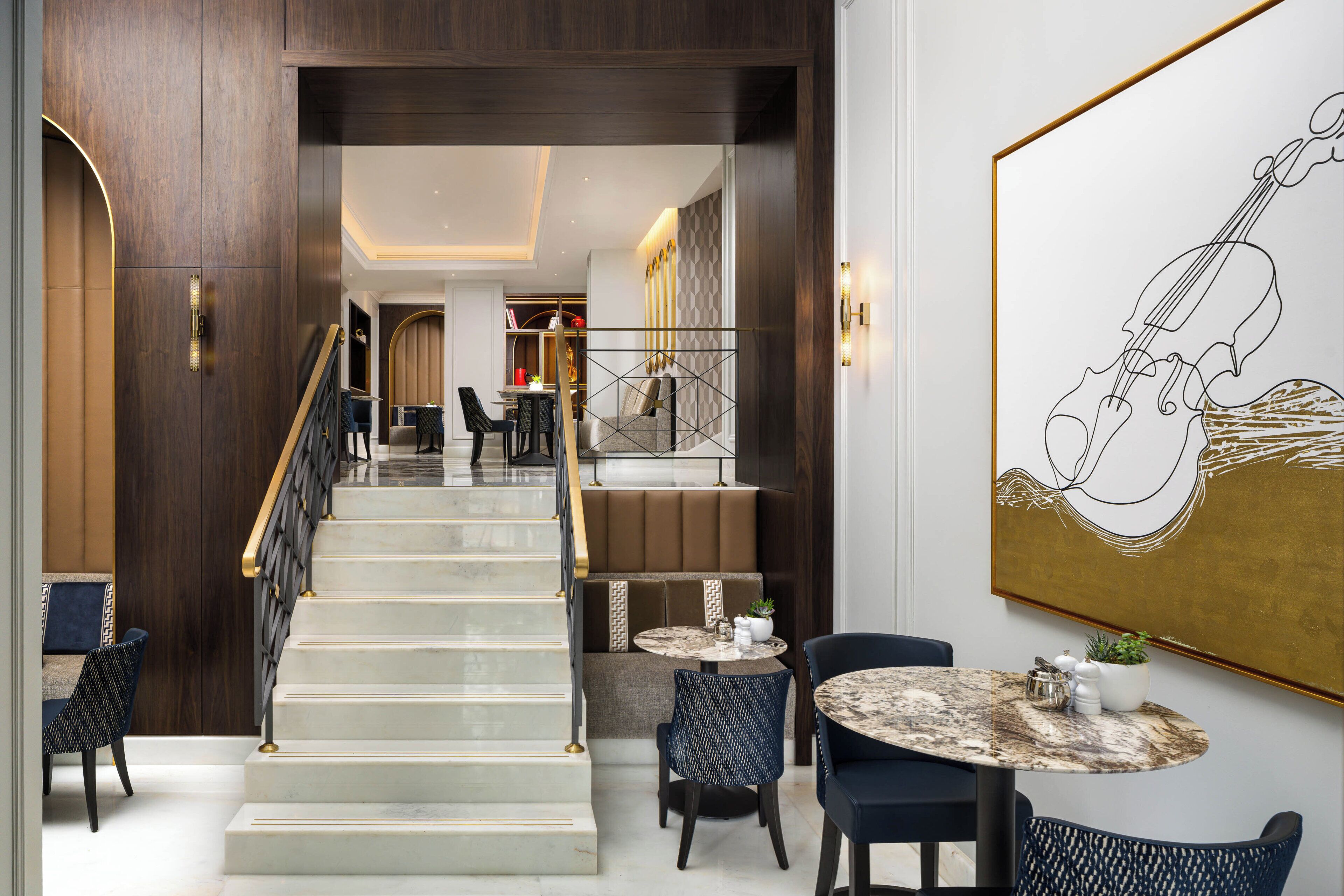 A modern hotel lobby with a marble staircase, seating area, and a large abstract painting.
