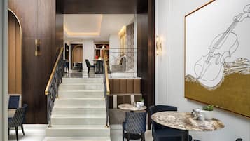 A modern hotel lobby with a marble staircase, seating area, and a large abstract painting.