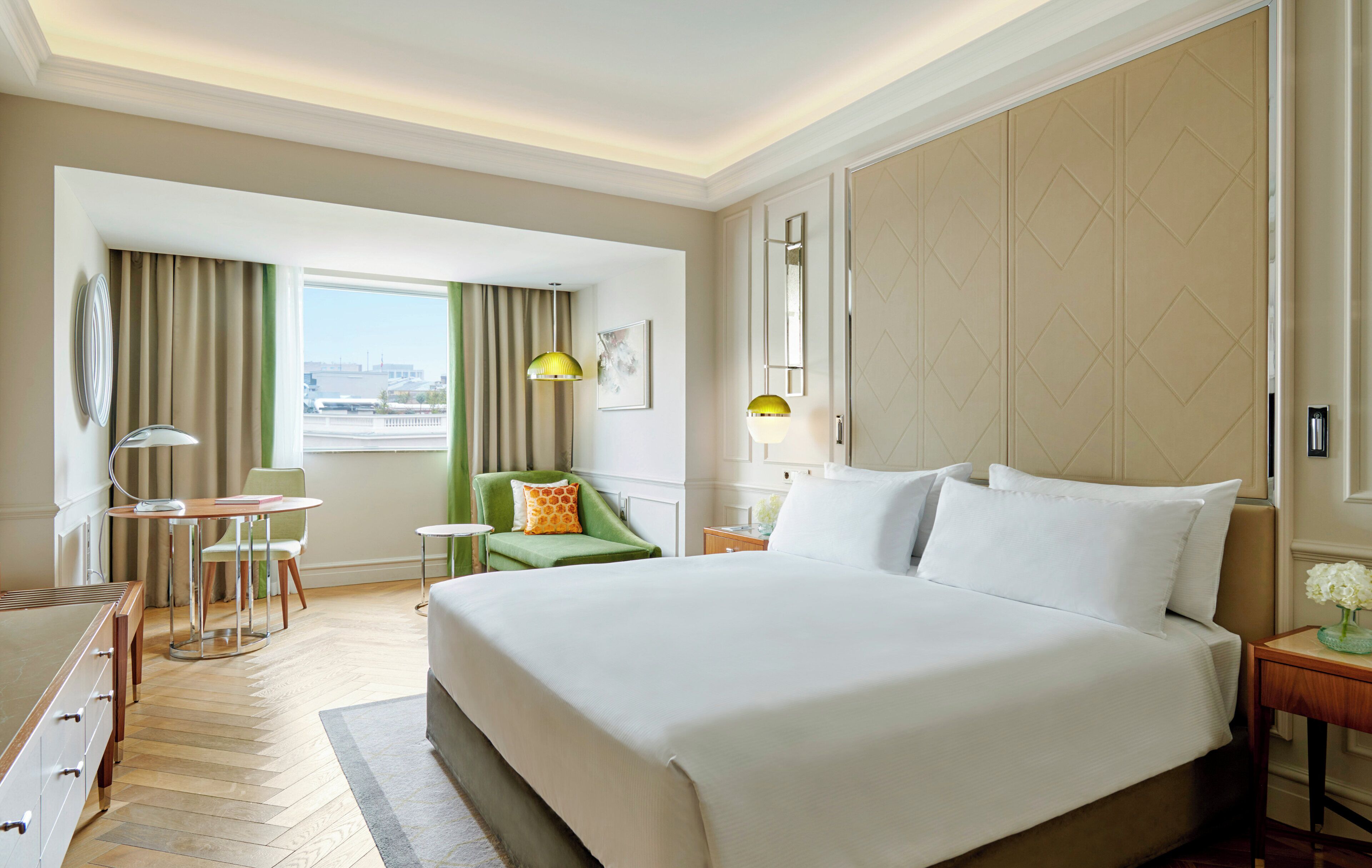 Une chambre d’hôtel avec un grand lit, un bureau, une chaise, une lampe et une vue sur la ville par la fenêtre.