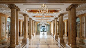 A grand hallway with marble columns, a large chandelier, and a view into a room with a large window. - InterContinental Athénée Palace Bucharest by IHG (Bucharest)
