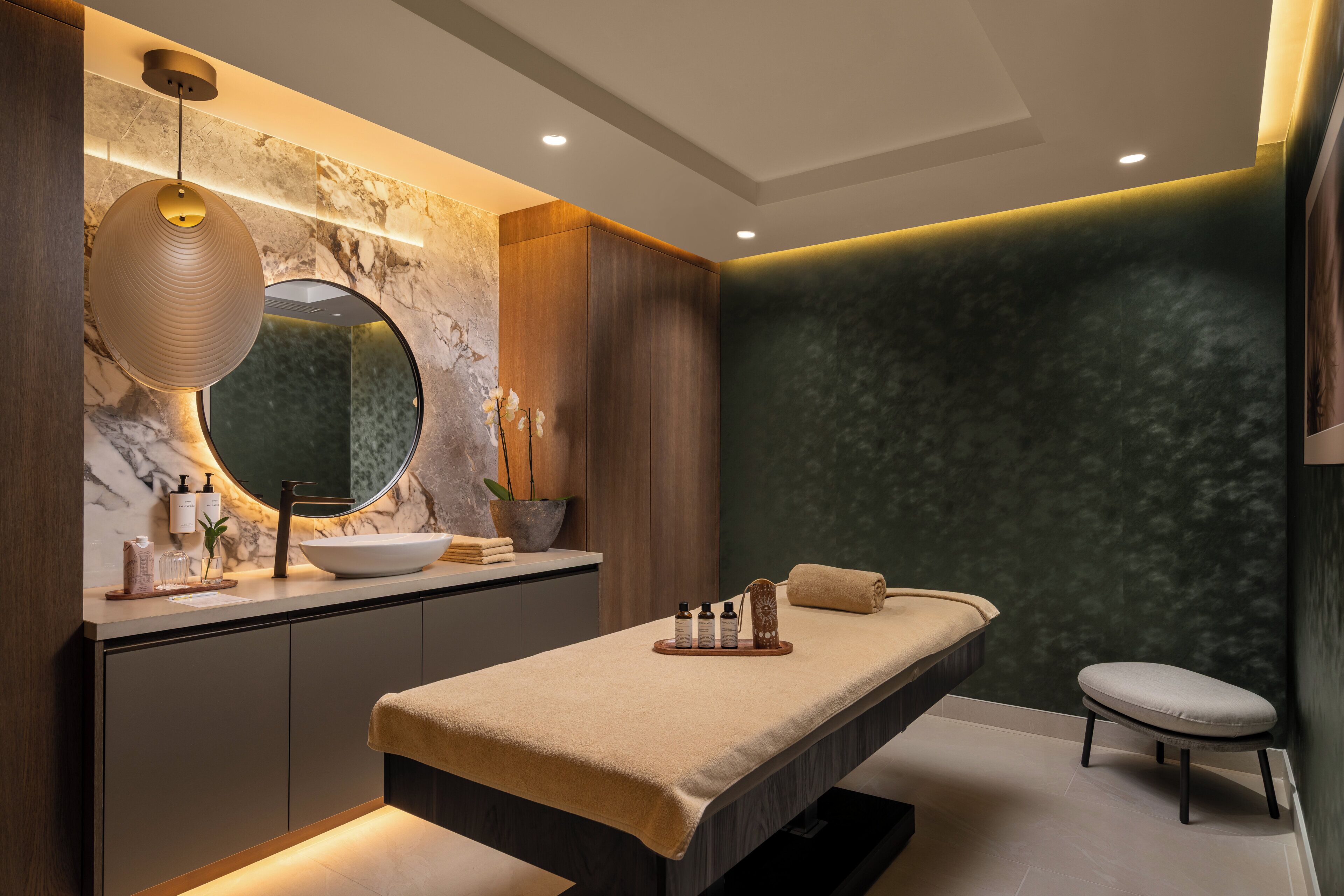 A modern bathroom with a marble vanity, a round mirror, and a massage table.