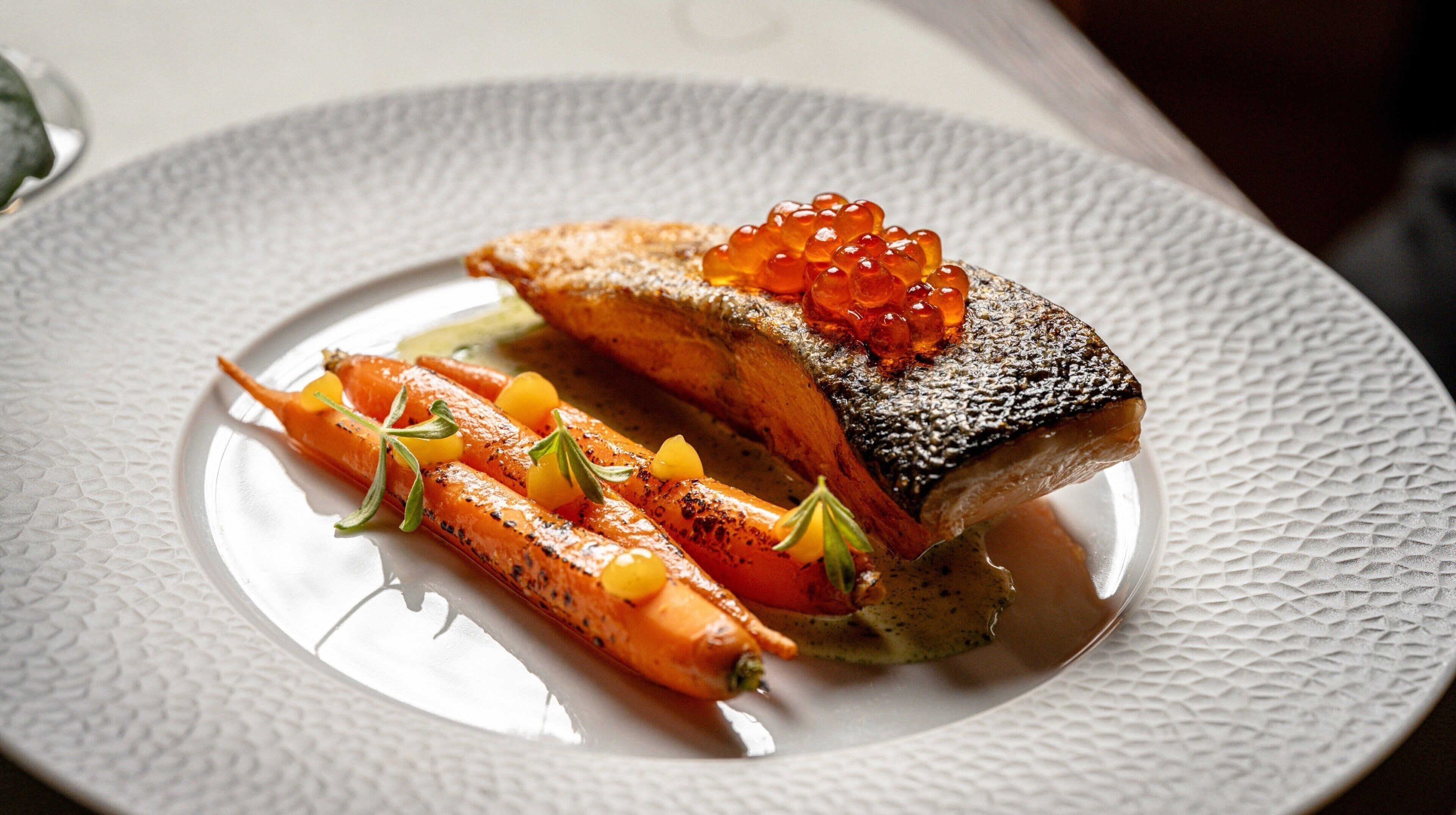 A plate with a piece of fish, carrots, and caviar.