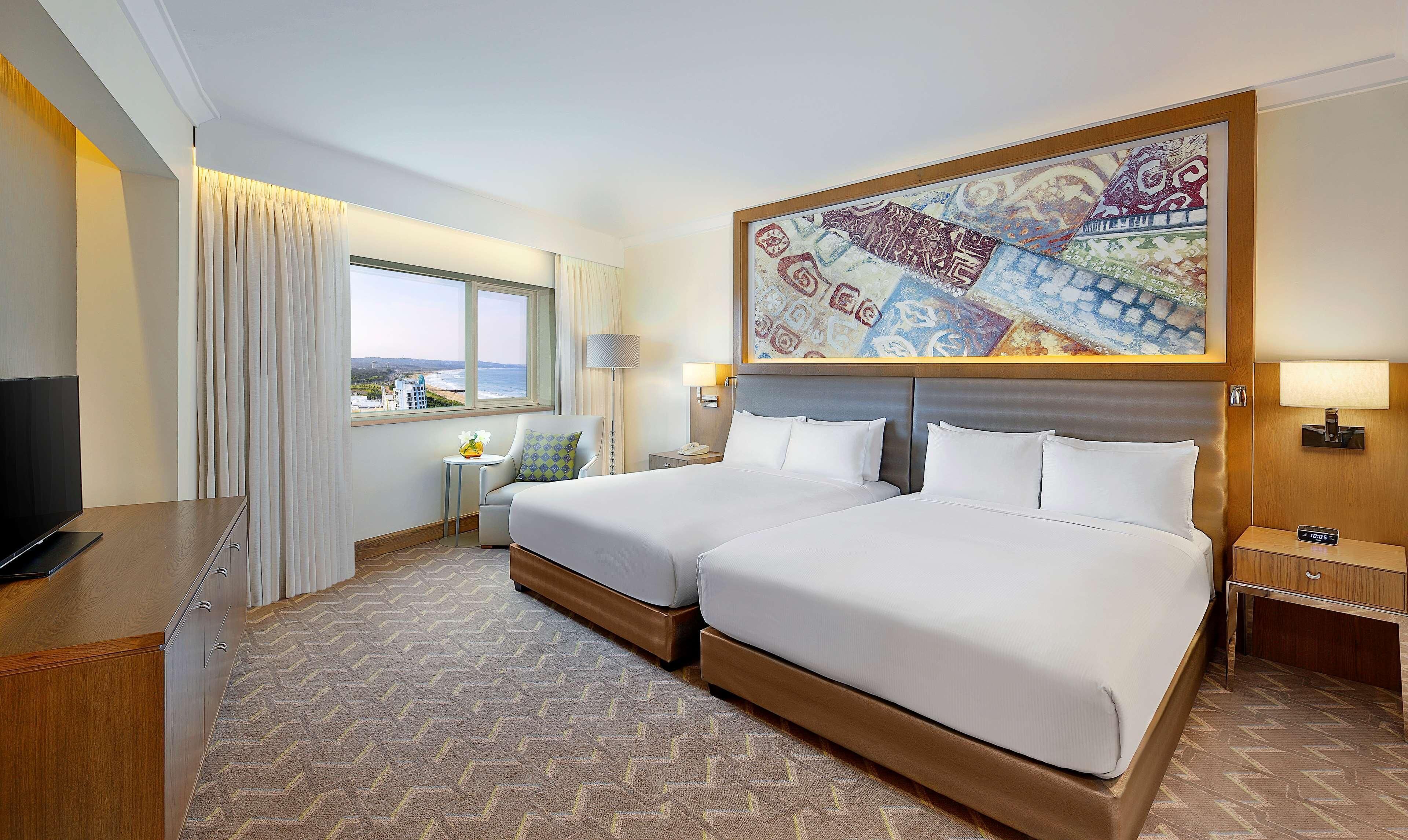A hotel room with a large bed, a television, a desk, and a window with a view.