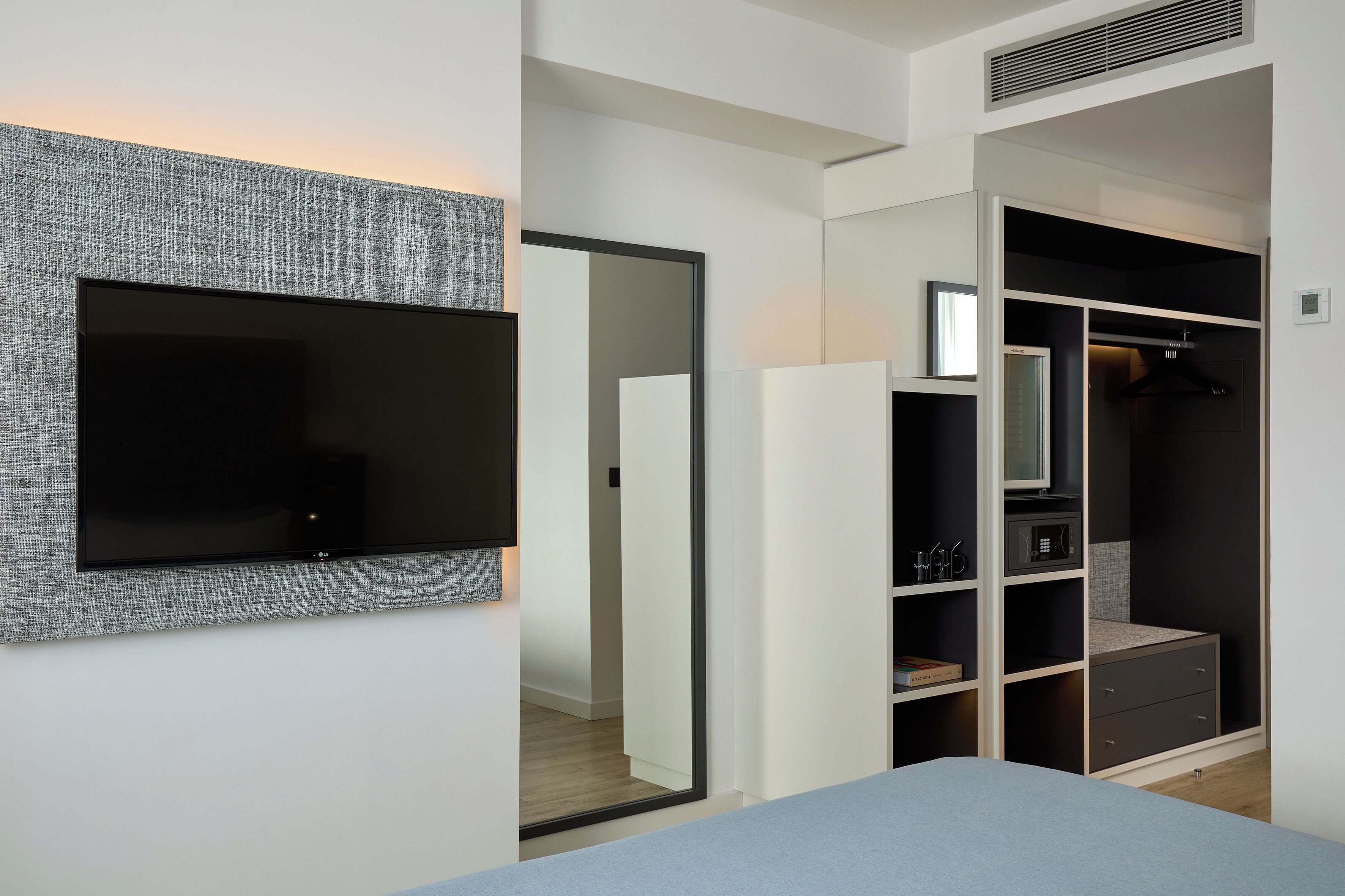 A modern bedroom with a flat-screen TV mounted on the wall, a walk-in closet with a mirror, and a bedside table.