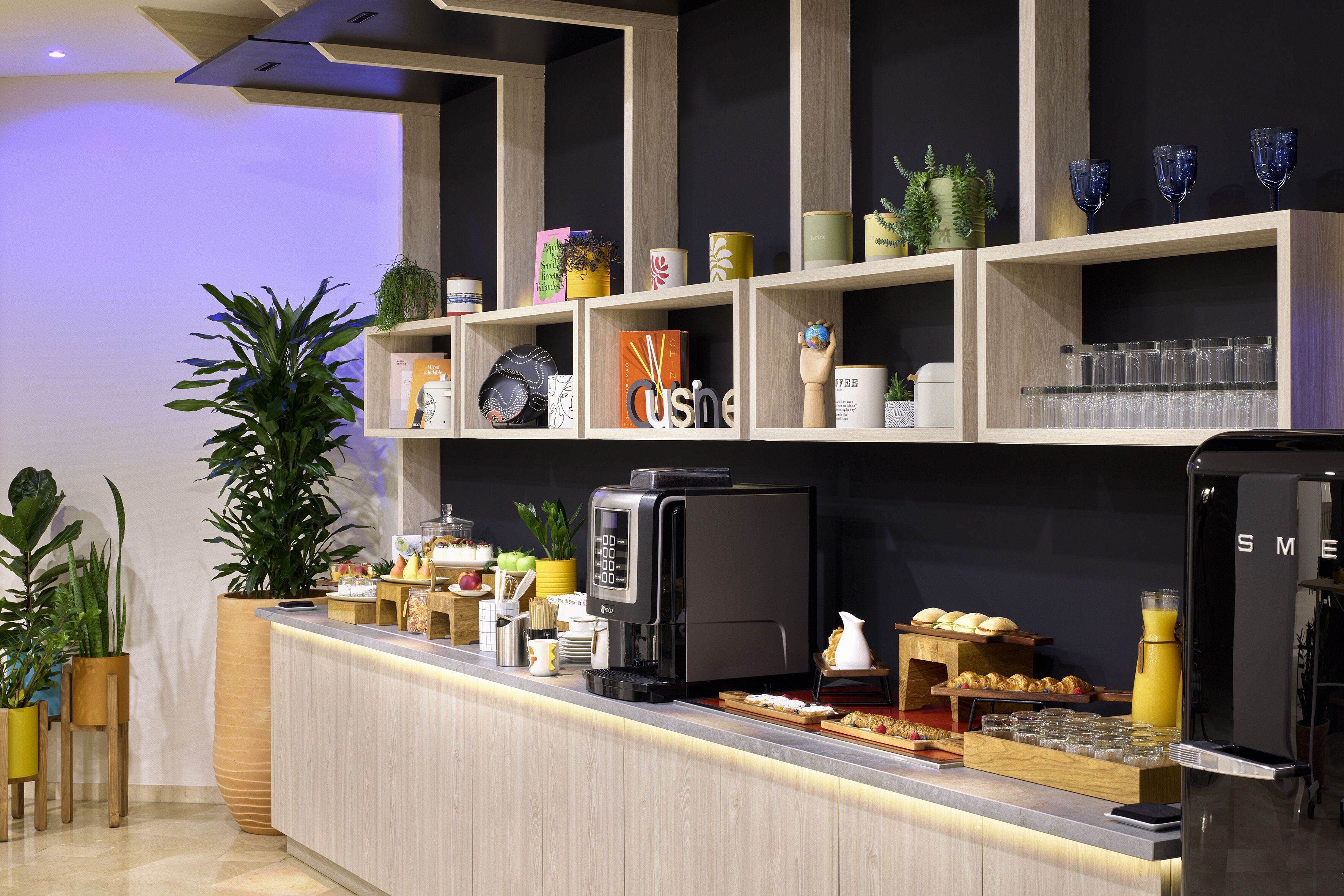A modern reception area with a coffee station, shelves with decorative items, and a refrigerator.
