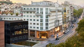 Um hotel moderno com fachada de vidro, um pátio e vista para a paisagem urbana.