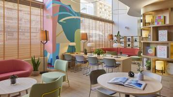 Un moderno vestíbulo de hotel con un área de comedor central, asientos cómodos y un mural vibrante.