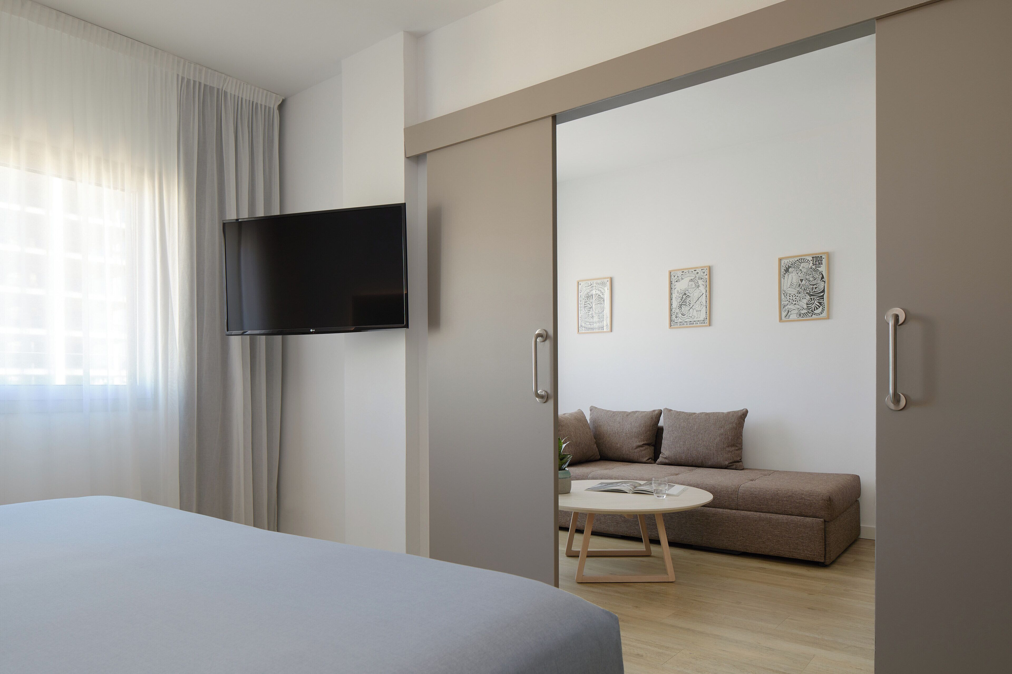 Habitació d'hotel moderna amb un llit, un televisor fixat a la paret, un sofà i una taula petita.
