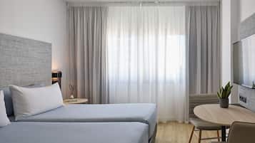 A hotel room with two beds, a TV, a small table with a plant, and a window with curtains.