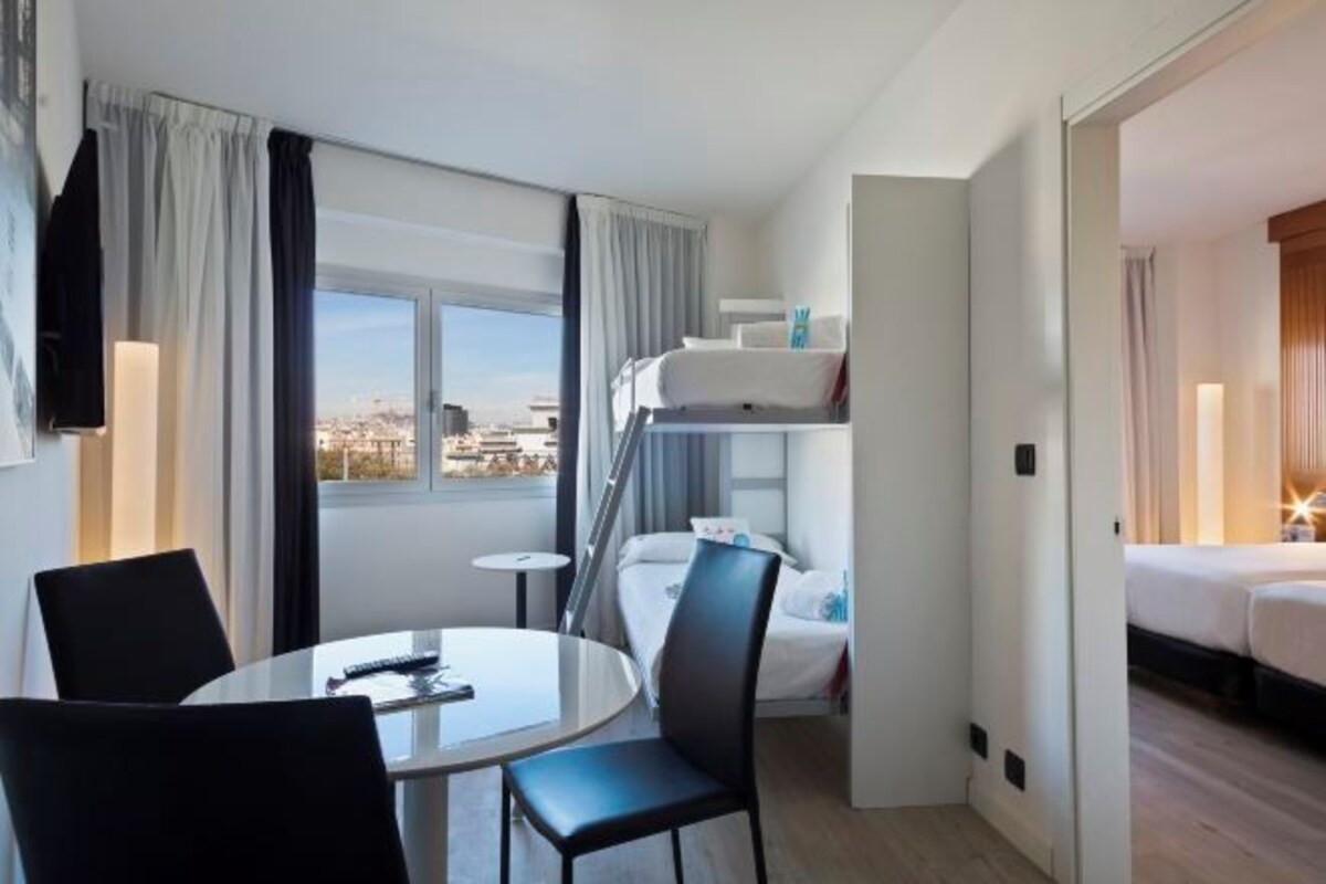 Hotellihuone, jossa on kerrossänky, pyöreä ruokapöytä tuoleineen, pieni sivupöytä ja näkymä kaupunkiin.