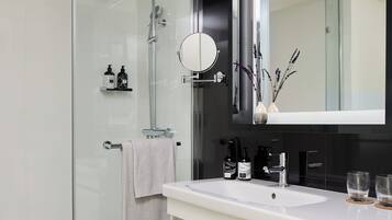 Un baño moderno con cabina de ducha de vidrio, un espejo grande y un tocador blanco con lavamanos.