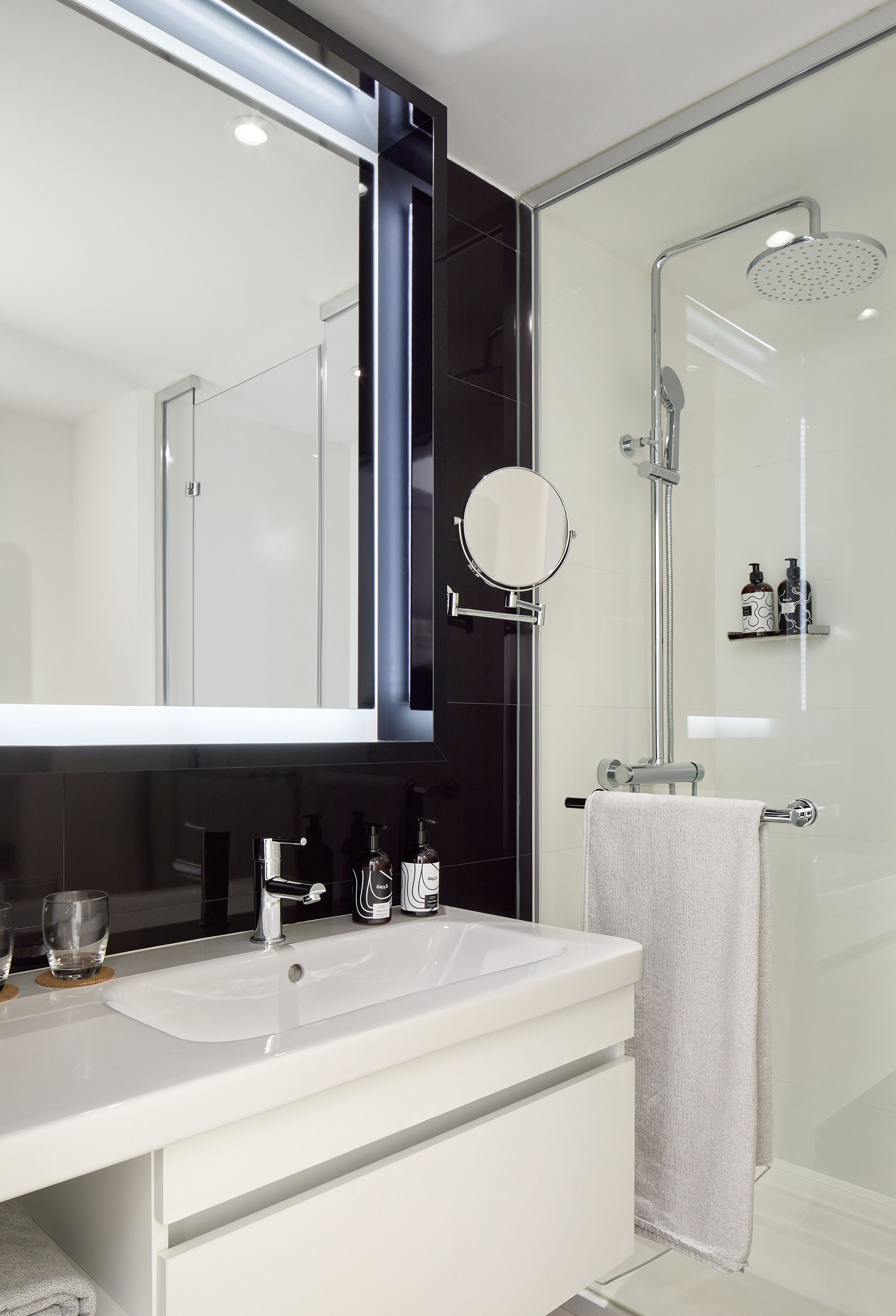 A modern bathroom with a white sink, a large mirror, a glass shower enclosure, and a towel rack.