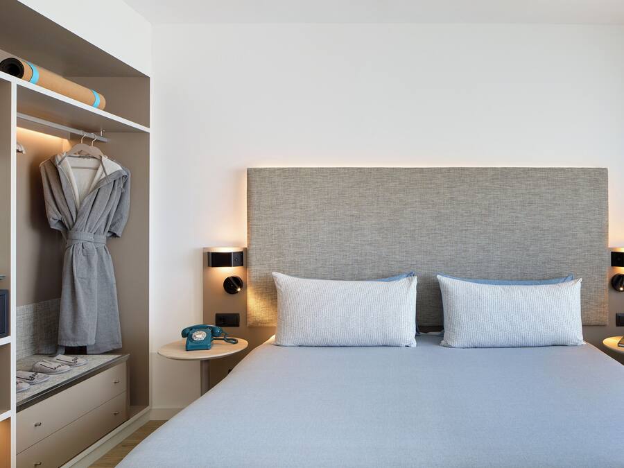 A hotel room with a bed, bedside tables, a robe hanging, and a television.