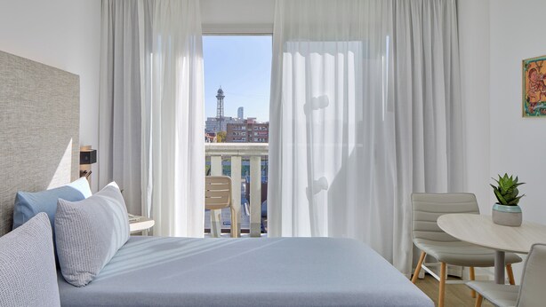 A hotel room with a bed, a desk, a chair, and a view of the cityscape through sheer curtains. - INNSiDE by Melia Barcelona Apolo (Barcelona)