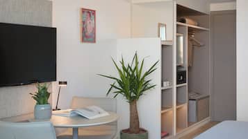 A modern hotel room with a flat-screen TV, a dining table, a potted plant, and a walk-in closet.