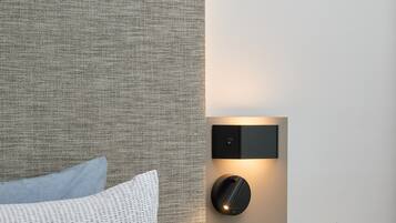 Une chambre moderne avec une tête de lit texturée, une table de chevet ornée d’une plante en pot, un livre et un luminaire fixé au mur.