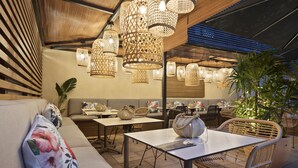 An outdoor dining area with wicker furniture, hanging lights, and a potted plant. - INNSiDE by Melia Barcelona Apolo (Barcelona)