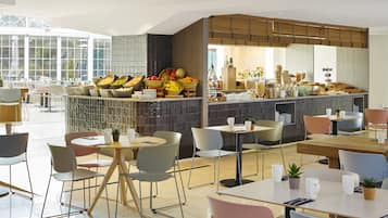 A modern cafe with a variety of seating options, a central bar area with fresh produce, and a bright interior with natural light.