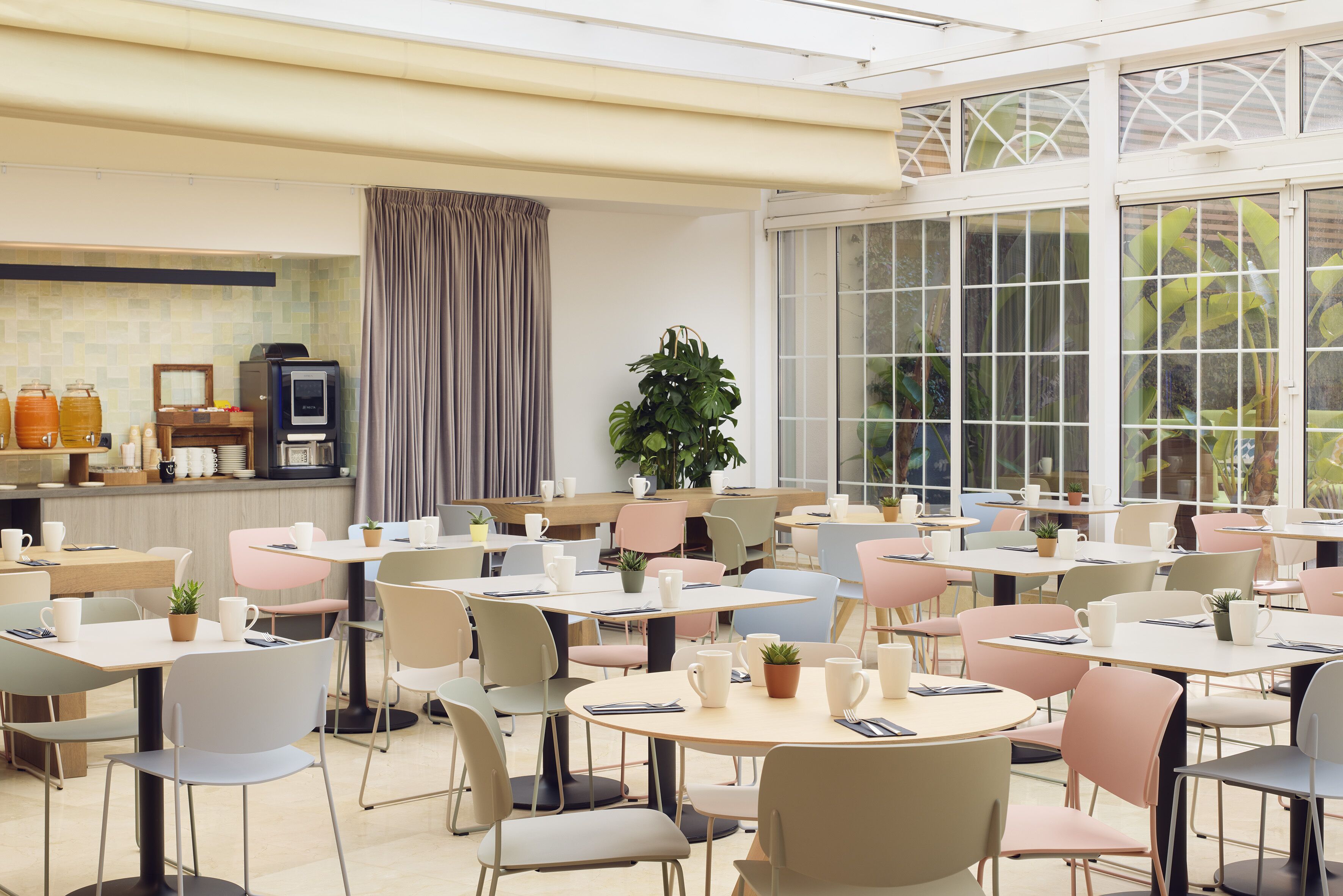 Ein geräumiges Café mit mehreren Tischen und Stühlen, einer Kaffeemaschine und einem großen Fenster mit Vorhängen.