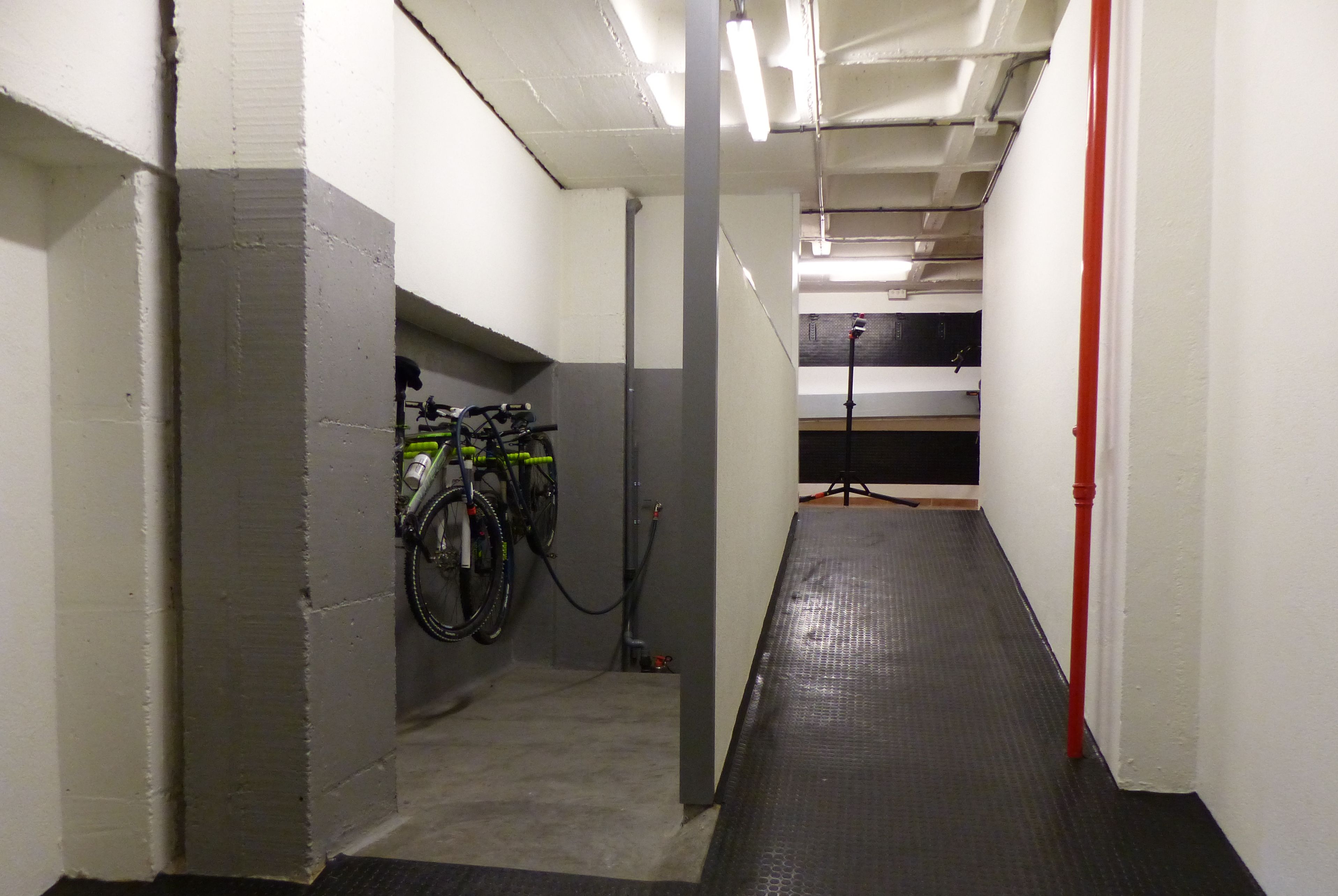 A narrow hallway with a bike rack on the left, a red pipe on the right, and a microphone stand in the distance.