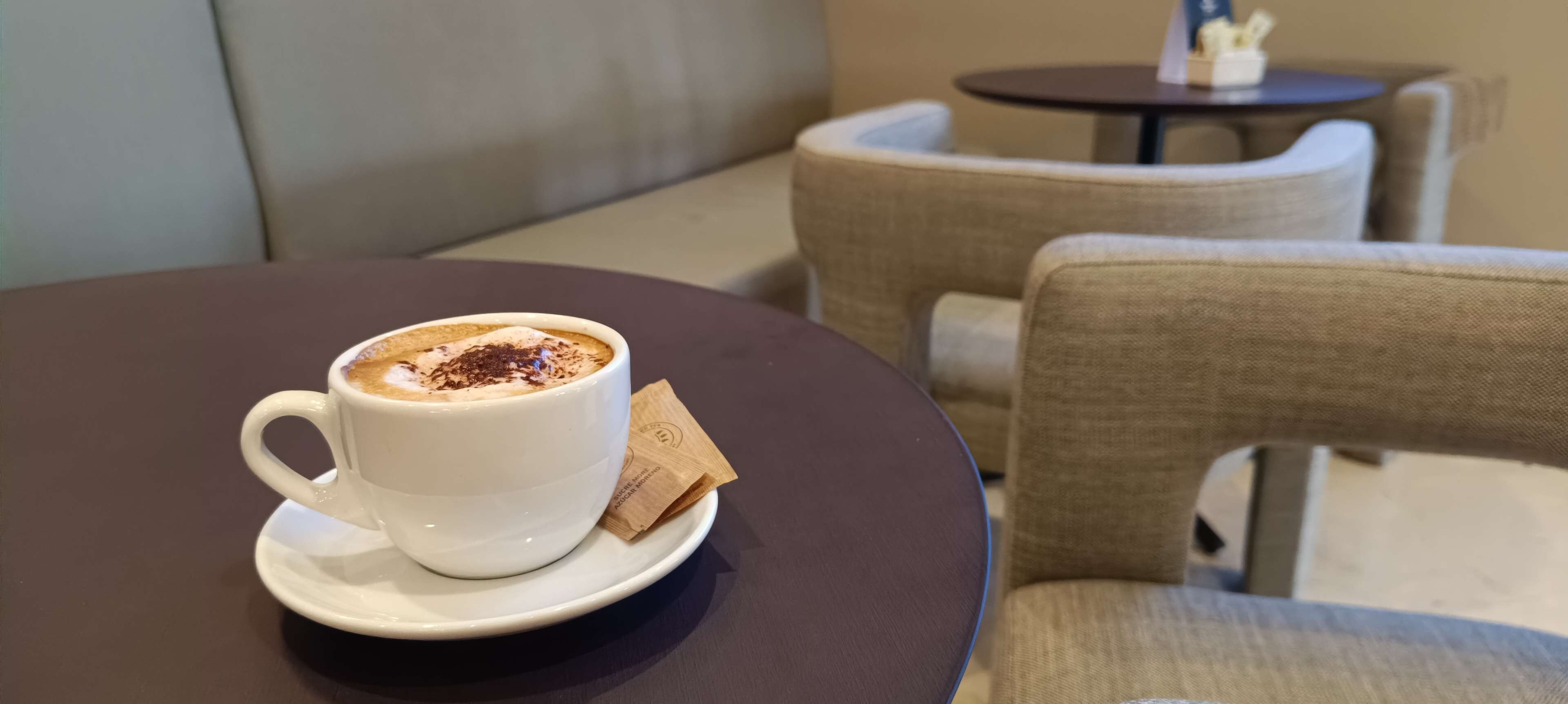 Una taza blanca de café con cobertura de chocolate sobre un plato, colocada sobre una mesa redonda.