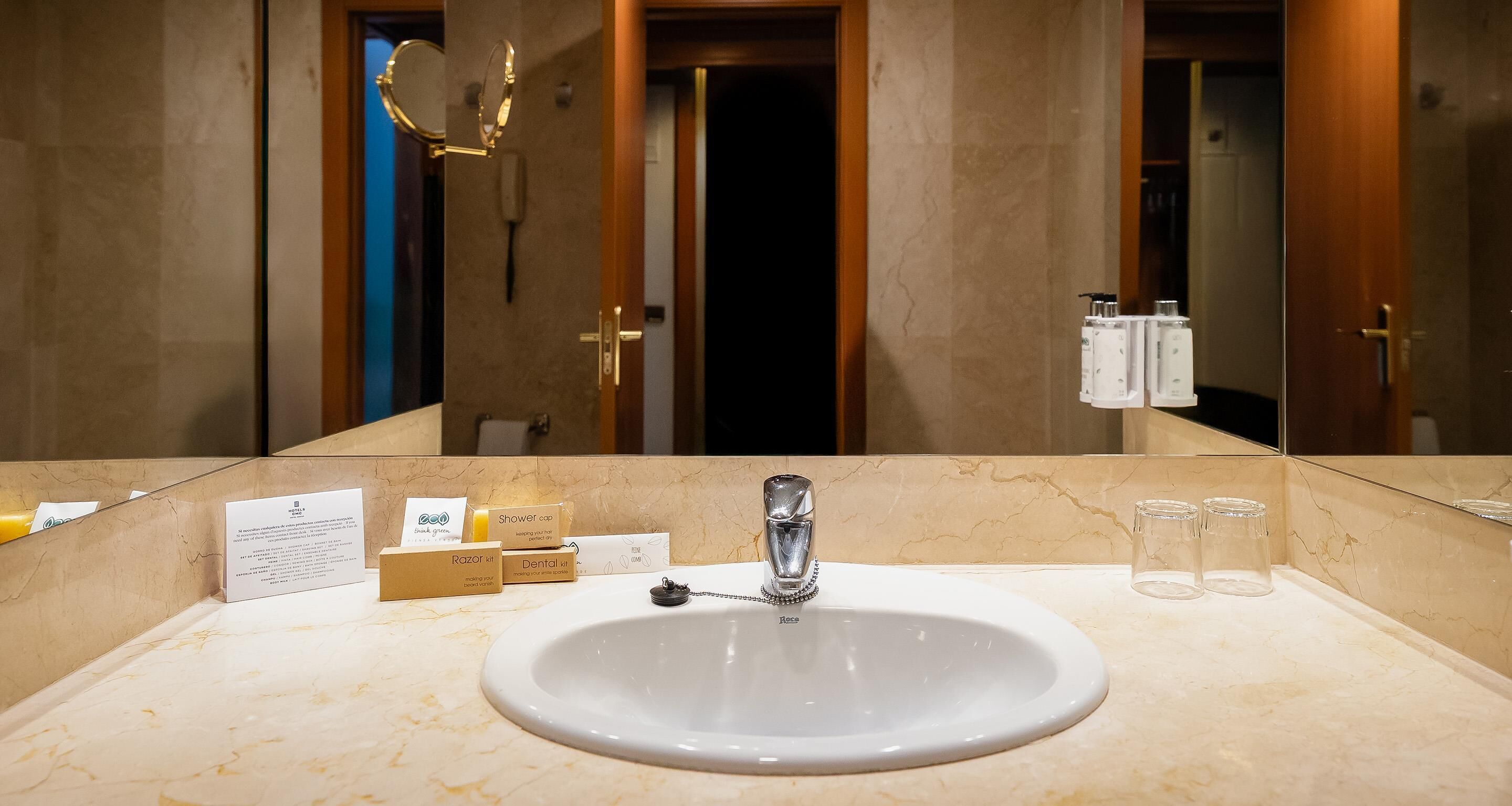 A hotel bathroom with a marble sink, a mirror, and toiletries on the counter.