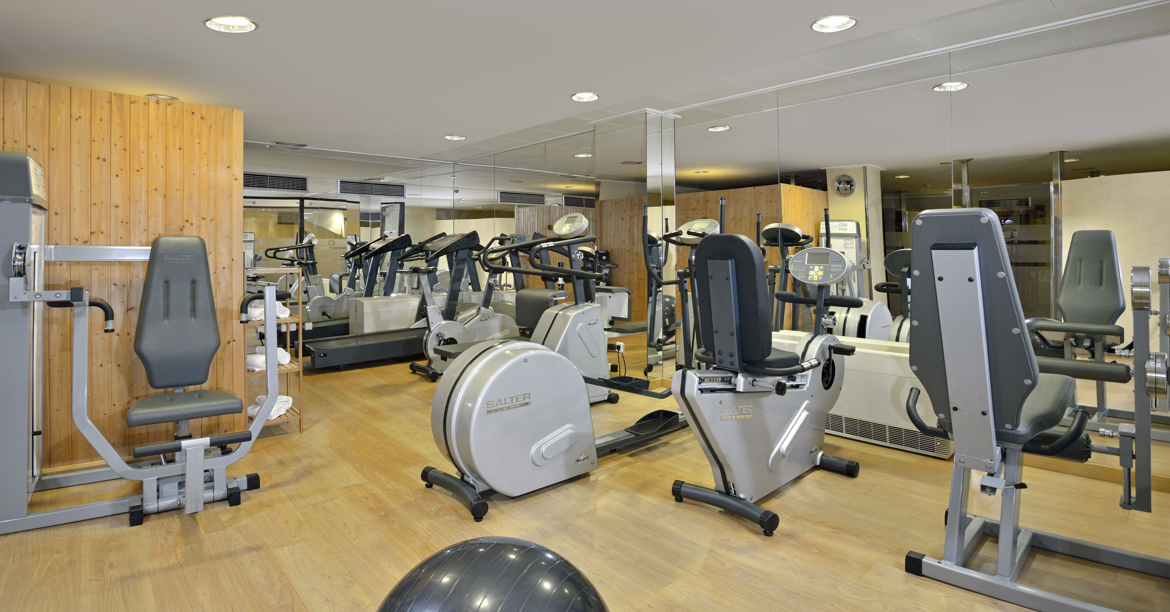 Une salle de sport équipée de divers appareils d’exercice, notamment des tapis de course et des appareils de musculation, avec un mur en bois en arrière-plan.