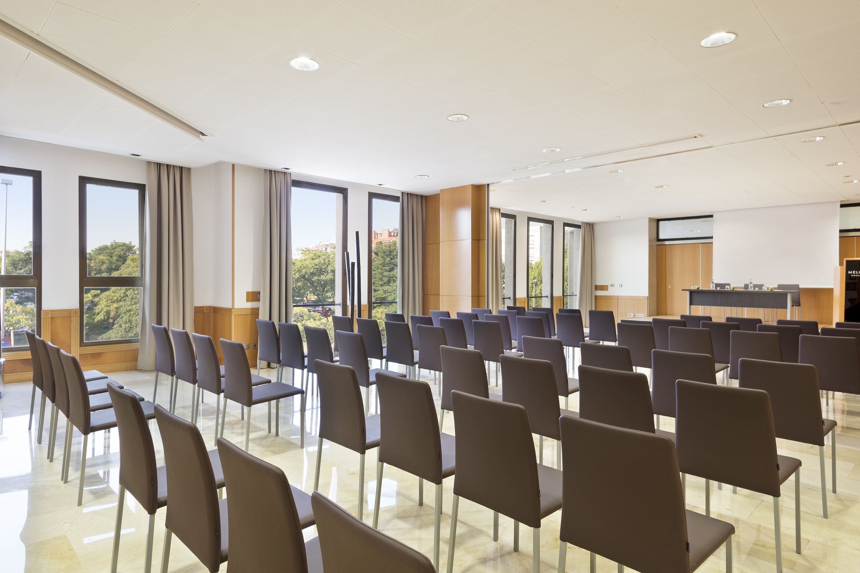 Ein Konferenzraum mit Reihen von Stühlen, großen Fenstern und einem Rednerpult.