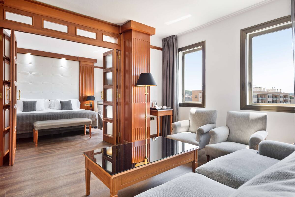 A modern hotel room with a bed, a sofa, a coffee table, and a view of the city.