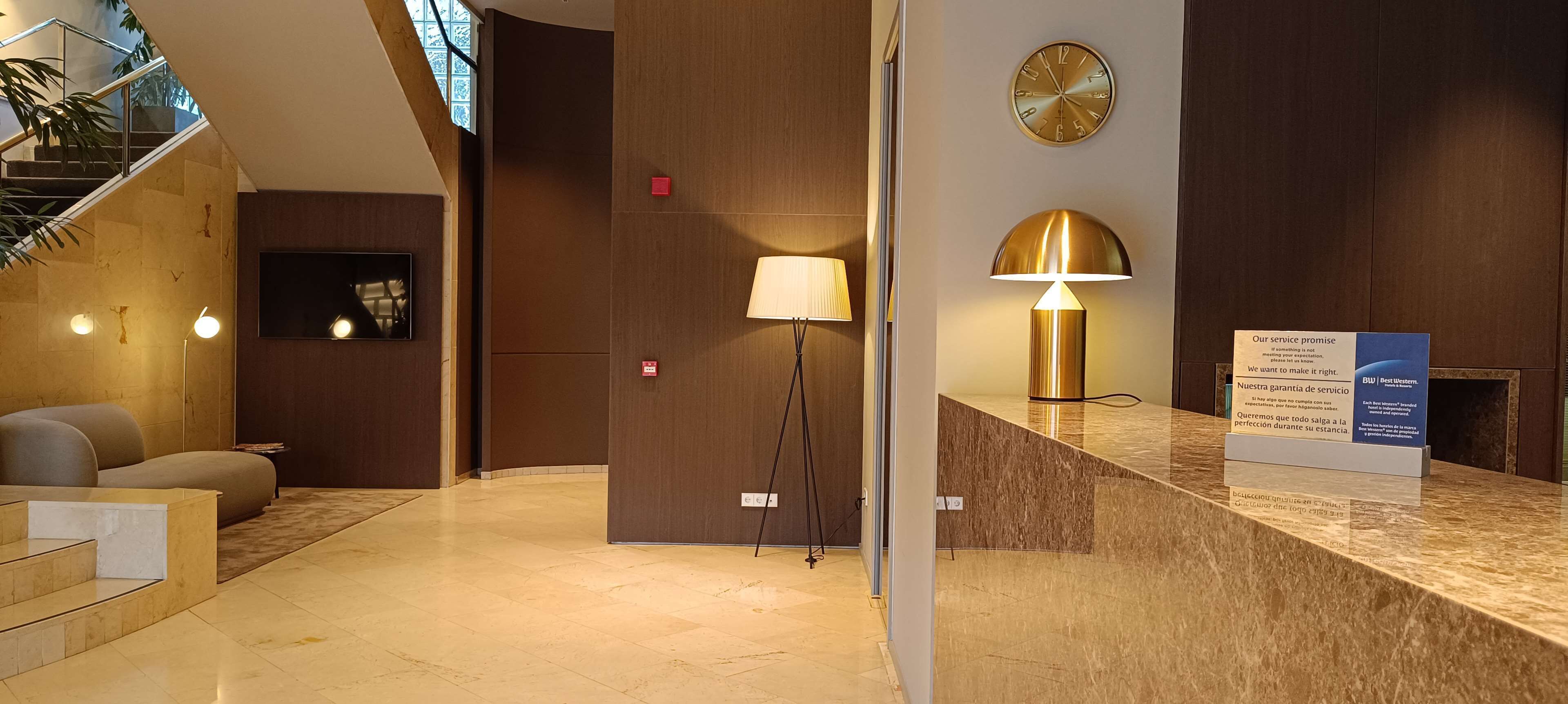 A modern lobby with a reception desk, a lamp, a clock, and a staircase.