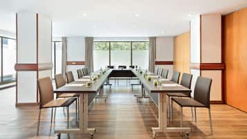 Un salón de conferencias con una larga mesa, sillas y vistas a árboles a través de amplias ventanas.