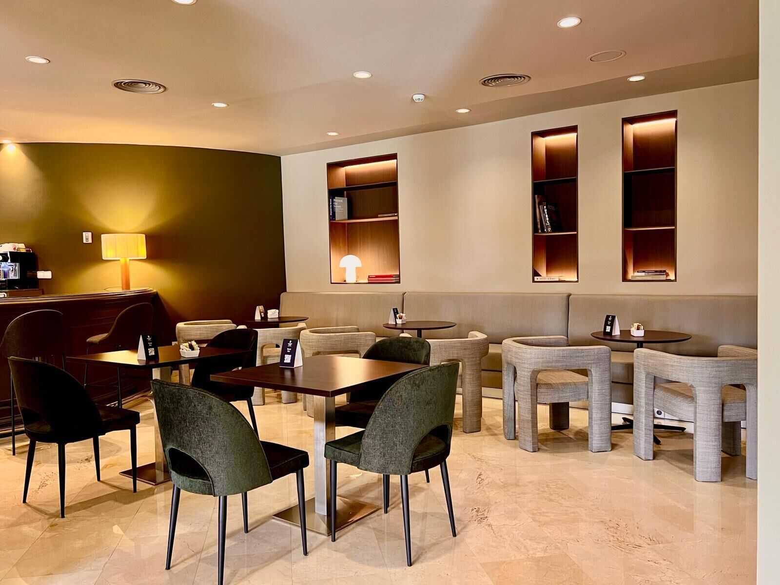 A modern hotel lobby with a seating area, tables, and a coffee machine.