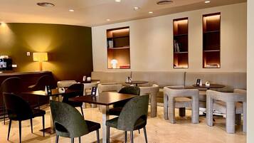 Um saguão de hotel moderno com área de estar, mesas e uma máquina de café.