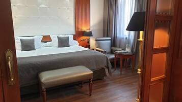 A hotel room with a large bed, a bench, a chair, a small table, and a lamp.