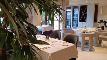 A restaurant with round tables, chairs, and a large potted plant in the foreground.